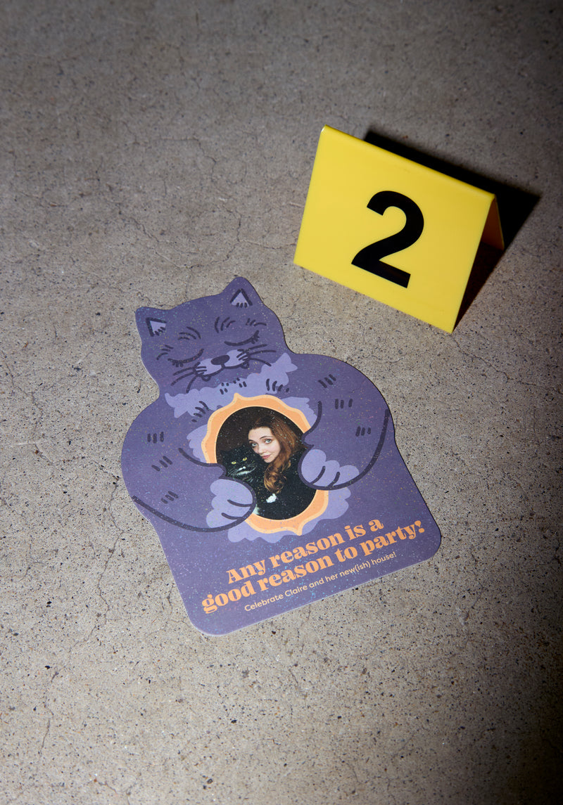 Plastic triangle marker with number 2 next to a party invite in the shape of a cat