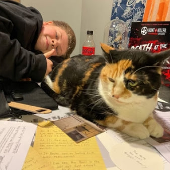 A happy boy and a cat with clues and case on a table on Hunt A Killer